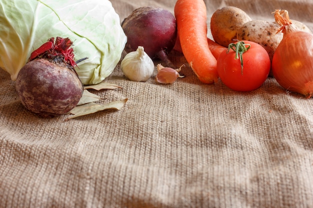 Vegetais crus para o borscht da sopa da beterraba. Repolho branco, beterraba, cenoura, batata, tomate, alho em uma placa de madeira