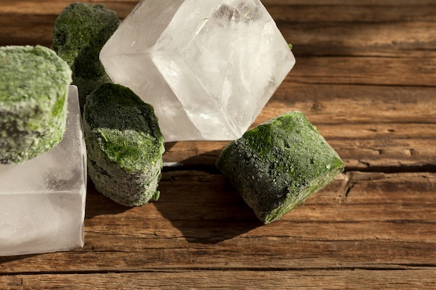 Vegetais verdes congelados, cubos de gelo e um copo transparente em uma velha mesa de madeira