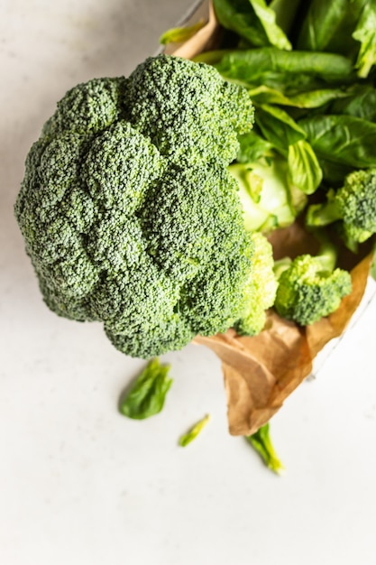 Foto vegetais verdes saudáveis com brócolis e espinafre em uma bandeja de madeira.