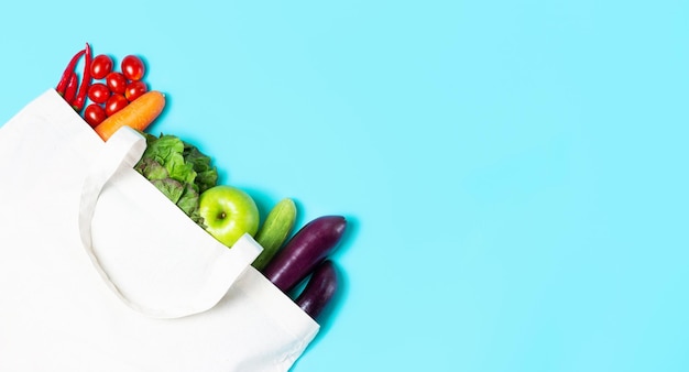 Vegetales y frutas multicolores en una bolsa de lino blanco sobre un fondo azul