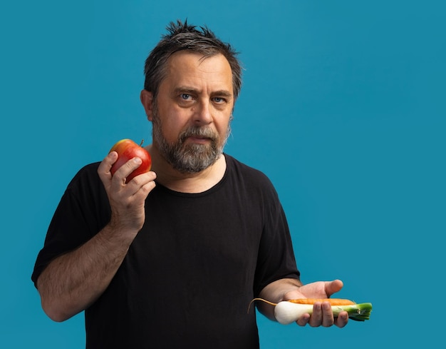 Vegetarianismo y estilo de vida saludable. Un hombre de mediana edad con una camiseta negra tiene frutas y verduras en sus manos