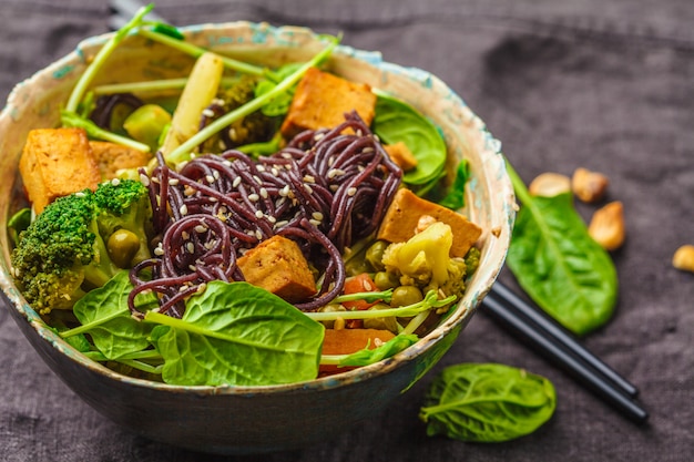 Vegetariano asiático salteado con tofu, fideos de arroz y verduras, fondo oscuro.