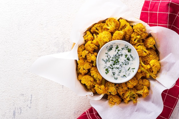 Vegetarisch gebackener Blumenkohl mit Semmelbröseln und Gewürzen mit Sauerrahmsauce und Gemüse auf weißem Hintergrund. vegetarisches Snackkonzept