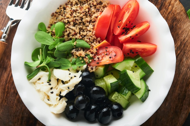 Vegetarisch Vegane Salatschüssel oder Buddha-Schüssel mit Tomaten-Gurken-Mozzarella-Käse-Quinoa-Oliven und Microgreens Gesundes und ausgewogenes Ernährungskonzept auf altem dunklem Holzhintergrund Kopierraum von oben