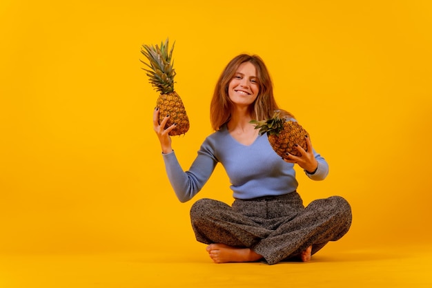 Vegetarische Frau, die mit einer geschnittenen Ananas lächelt, die sich hinsetzt, gesundes Leben und tropisches Fruchtkonzept