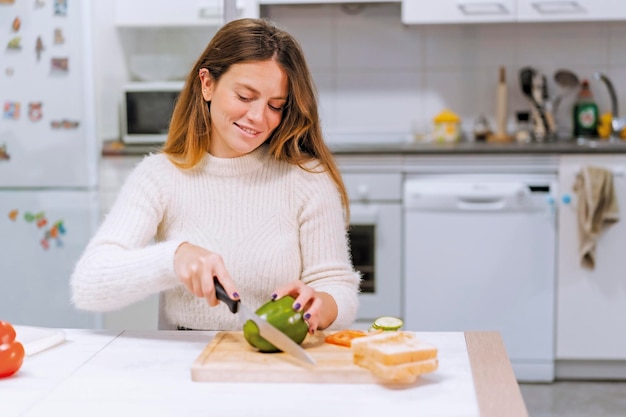 Vegetarische Frau, die zu Hause ein Gemüsesandwich in der Küche kocht und grünen Pfeffer schneidet