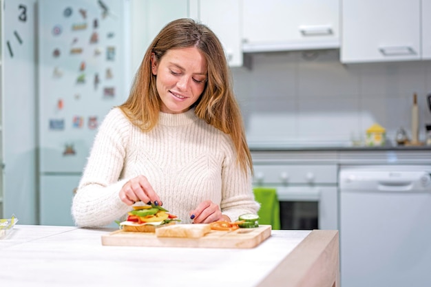 Vegetarische Frau, die zu Hause ein Gemüsesandwich in der Küche kocht Zubereitung durch Tomate