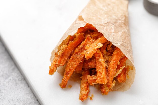 Vegetarische gesunde Bio-Lebensmittel Gesunder Snack Gebackene frittierte Karottensticks in Papier auf Marmorplatte