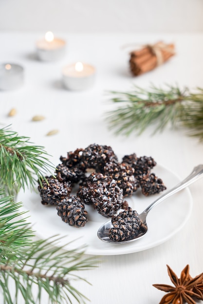 Vegetarische getrocknete Tannenzapfen auf Teller auf weißem Holztisch mit Tannenzweigen, Gewürzen und Kerzen