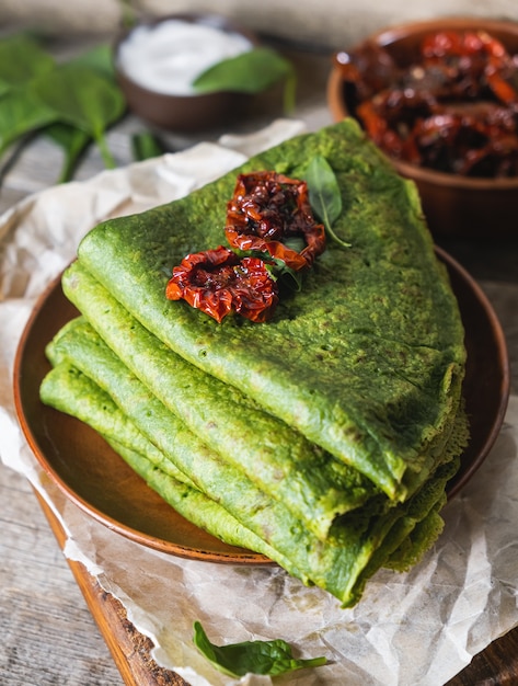 Vegetarische grüne Pfannkuchen verziert mit getrockneten Tomaten. Spinatpfannkuchen in einem braunen Teller auf einem Schreibtisch aus Holz.