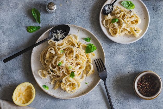 Vegetarische Nudeln mit Zitrone, Basilikum, Parmesan und schwarzem Pfeffer auf grauer Steinoberfläche. Draufsicht mit Kopierraum.