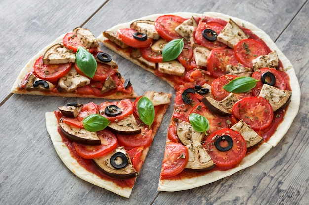 Vegetarische Pizza mit Aubergine, Tomate, schwarzen Oliven, Oregano und Basilikum auf Holztisch