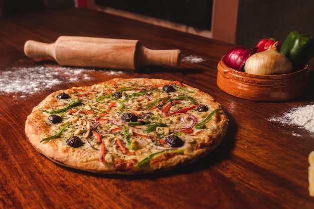 Vegetarische Pizza neben Gewürzen auf einem Holztisch.