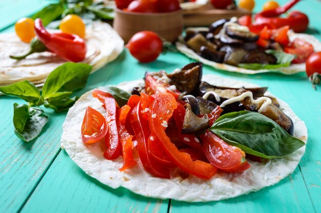 Vegetarische Tacos mit Auberginen, Kirschtomaten, Paprika auf hellem Holztisch