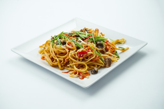 Vegetarische Udon-Nudeln in süß-saurer Sauce mit Gemüse in einem weißen Teller auf einem grauen Tisch. Nahansicht