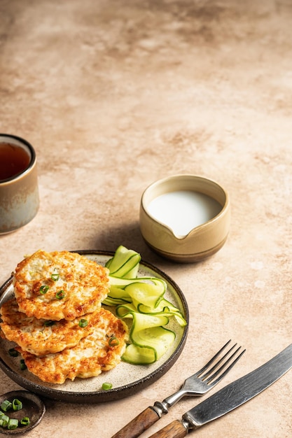 Vegetarische Zucchini-Krapfen mit Frühlingszwiebeln und Gurken, serviert mit Sahnesauce mit Besteck und Tee Textraum