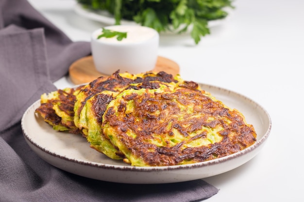 Vegetarische Zucchini-Krapfen oder Zucchini-Pfannkuchen, serviert mit frischen Kräutern und Sauerrahm.