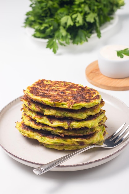 Vegetarische Zucchini-Krapfen oder Zucchini-Pfannkuchen, serviert mit frischen Kräutern und Sauerrahm.