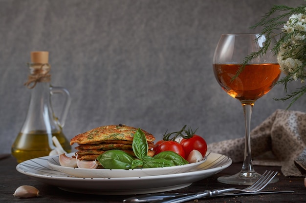 Vegetarische Zucchini-Krapfen, serviert mit frischen Kräutern, Tomaten und Knoblauch. Romantisches Abendessen mit Wein