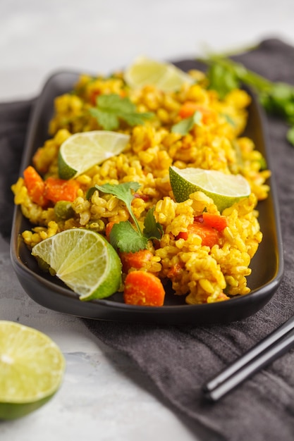 Vegetarischer Curryreis mit Gemüse und Kokoscreme in einer schwarzen Schale. Grauer Hintergrund, Kopierraum. Gesundes veganes Lebensmittelkonzept, Entgiftung, Gemüsediät.