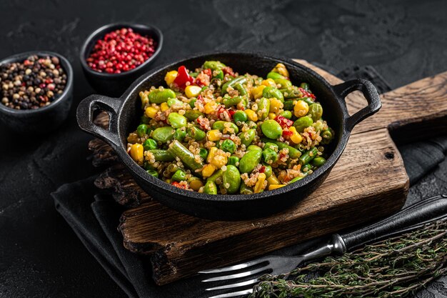 Vegetarischer gebratener Quinoa-Salat mit Edamame, Mais, Karotte, Tomate, Paprika, Zwiebeln in einer Pfanne. Schwarzer Hintergrund. Ansicht von oben.