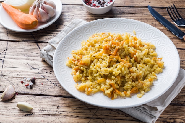 Vegetarischer orientalischer Pilaf mit Reis und Gemüse auf einem Holztisch.