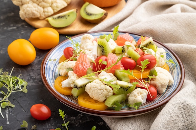 Vegetarischer Salat aus Blumenkohlkohl, Kiwi, Tomaten, mikrogrünen Sprossen auf Schwarz