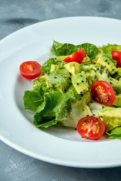 Vegetarischer Salat mit Avocado-, Salat- und Kirschtomaten in einem weißen Teller auf Beton