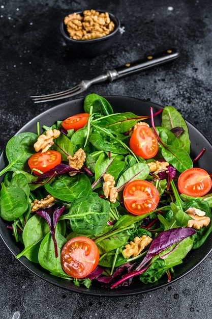 Vegetarischer Salat mit gemischten Blättern Mangold, Mangold, Spinat, Rucola und Nüssen in einer Salatschüssel. Schwarzer Hintergrund. Ansicht von oben.