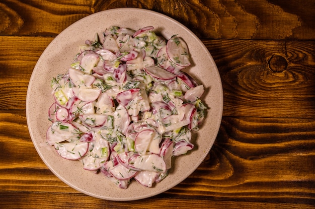 Vegetarischer Salat mit Rettich, Frühlingszwiebeln und Sauerrahm auf einer Keramikplatte. Ansicht von oben