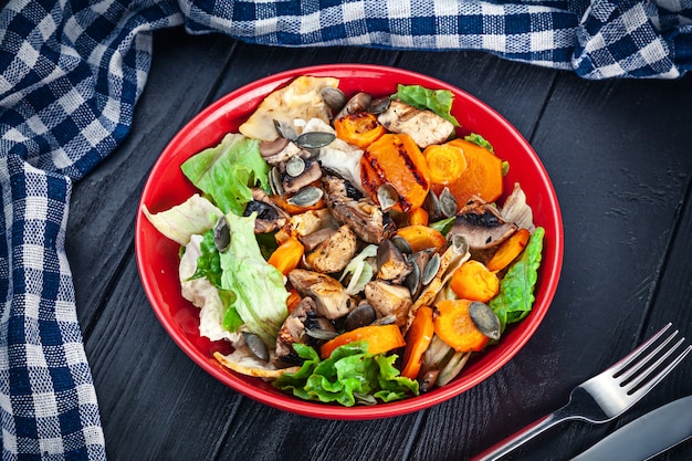 Vegetarischer Salat von Karotten, Pilzen, Salat in Orangenschale auf dunkler Holzoberfläche