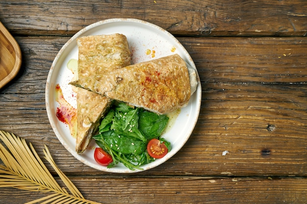 Vegetarisches Dönerbrötchen mit Spinat, Tomaten, Hummus und geschmolzenem Käse in einem Teller auf einem Holz