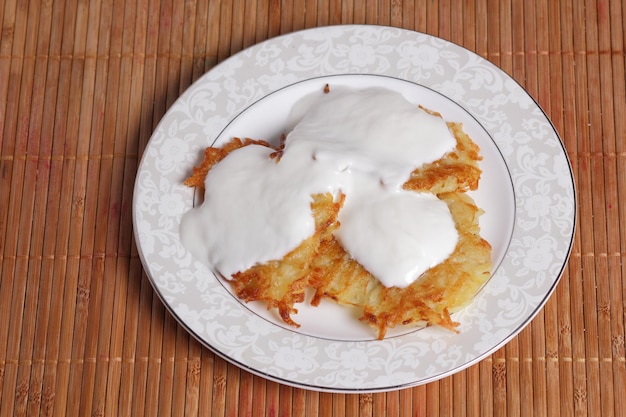 Vegetarisches Essenskonzept Fertige hausgemachte Kartoffelpuffer mit Sauerrahm auf einem weißen Teller auf Holzhintergrund Nahaufnahme