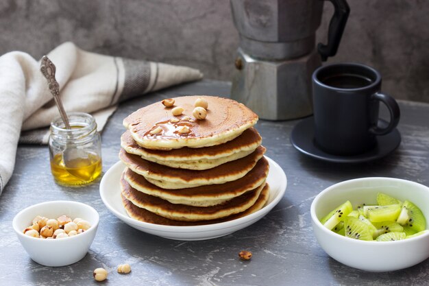 Vegetarisches Frühstück mit Pfannkuchen, Kaffee, Honig, Nüssen und Früchten.