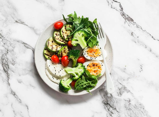 Vegetarisches Frühstück Schüssel Salat gemischtes Gemüse gekochtes Ei gegrillter Zucchini-Käse auf hellem Hintergrund Blick über