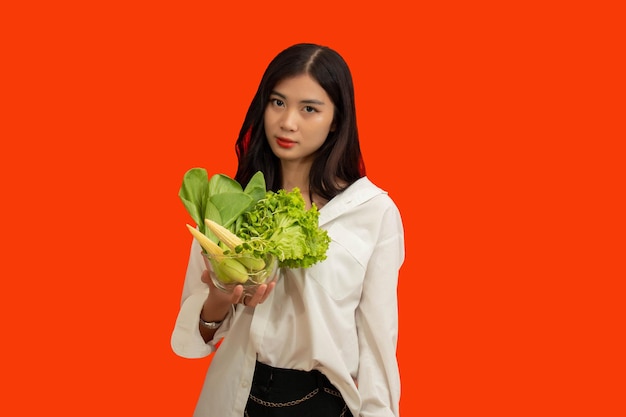 Vegetarisches Konzept Gesunde Frau, die eine Schüssel mit frischem Gemüse auf orangefarbenem Hintergrund isoliert hält