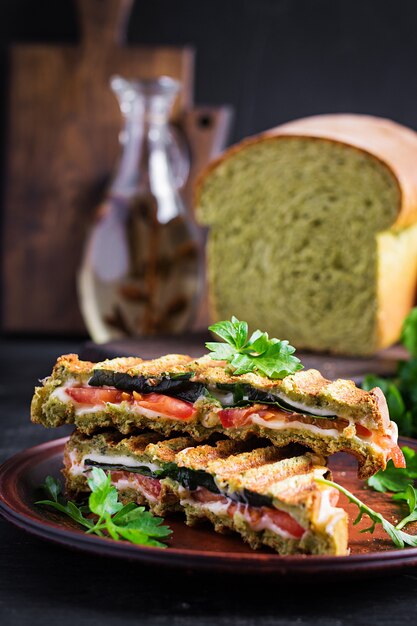 Vegetarisches Sandwich Panini mit Spinatblättern, Tomaten und Käse auf einem dunklen Tisch. Toast mit Käse.