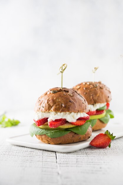 Veggie, hamburguesa vegana con fresa, pera, requesón y espinacas en pan fresco con semillas de calabaza en pizarra.