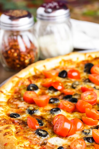 Veggie-Pizza mit Oliven und Kirschtomaten auf dem Tisch.