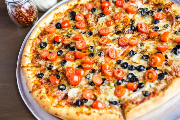 Veggie-Pizza mit Oliven und Kirschtomaten auf dem Tisch.