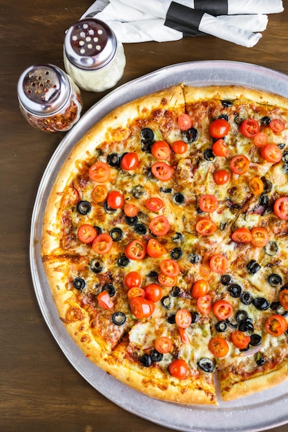 Veggie-Pizza mit Oliven und Kirschtomaten auf dem Tisch.