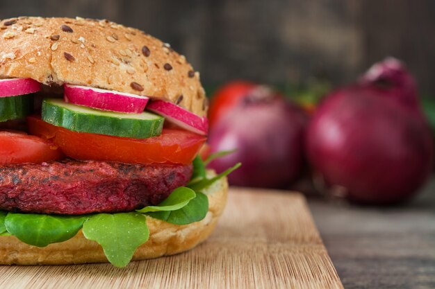 Veggie-Rüben-Burger mit Lammsalat, Tomate, Radieschen und Gurke auf rustikaler Holzoberfläche