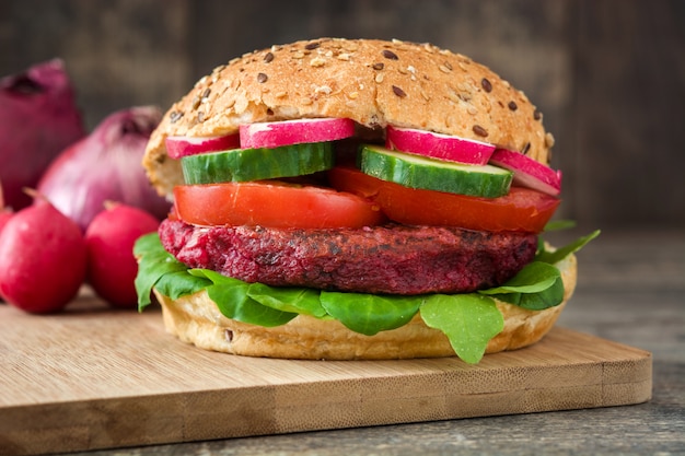 Veggie-Rüben-Burger mit Lammsalat, Tomate, Radieschen und Gurke auf rustikaler Holzoberfläche