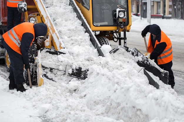 El vehículo cargador de garras quita la nieve de la carretera. Empleados de los servicios municipales ayudan a palear la nieve