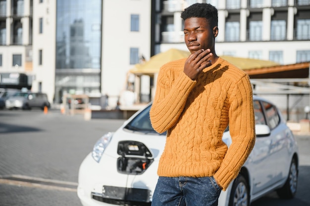 Vehículo eléctrico urbano, concepto ecológico. Joven de piel negra, esperando la carga de su coche eléctrico