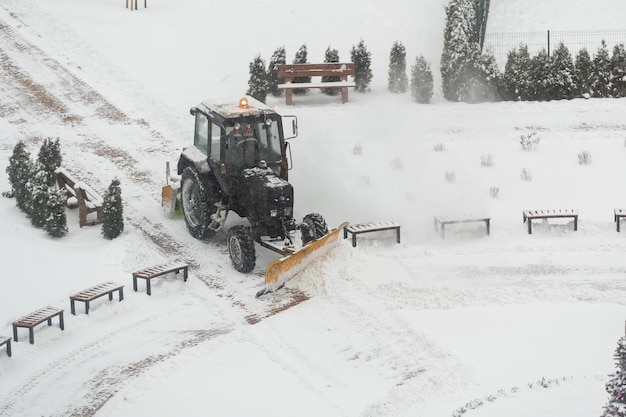 Vehículo tractor limpiando el patio de la tormenta de nieve, quitanieves quita la nieve en el patio