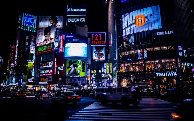 Vehículos en la calle contra vallas publicitarias iluminadas en edificios en Shibuya