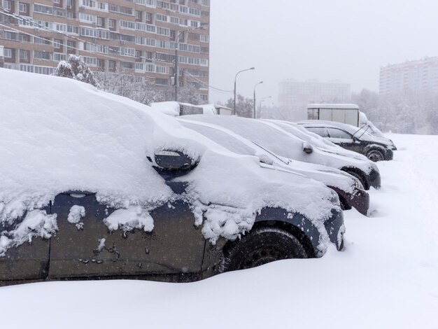 Foto vehículos cubiertos de nieve en la ventisca invernal en el estacionamiento