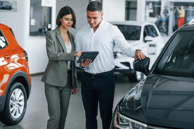 Veículos modernos Homem com roupa formal, ajudando o cliente na escolha do automóvel
