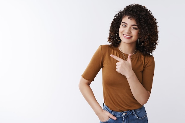 Foto veja você mesmo uma venda maluca. mulher alegre, agradável, de cabelos cacheados, caucasiano, elegante, mulher, convidativo, produto check-out, sugira, olhar para a esquerda apontando para o lado dedo indicador sorrindo encantado, fundo branco